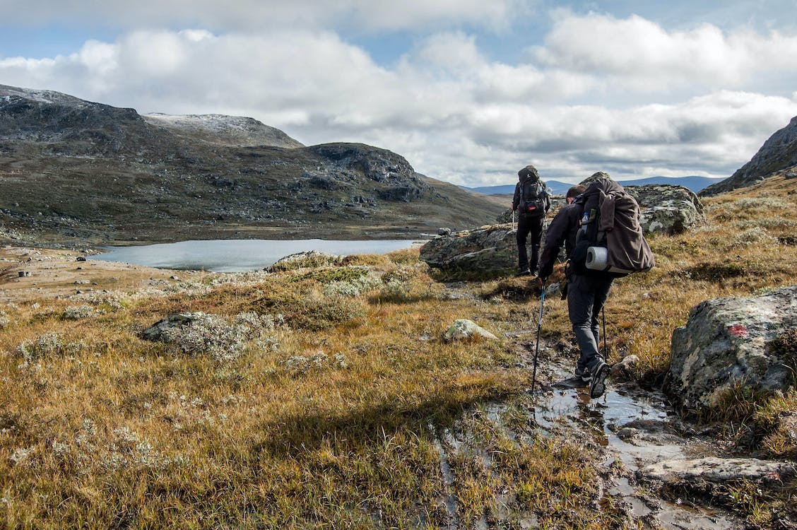 A group of people trekking through a grassy mountainous region.